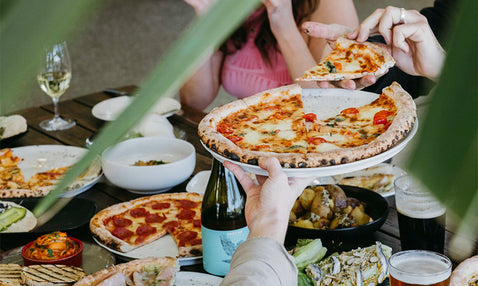 A plate of pizza being passed around at a table full of food, beer and wine at Eagle Bay Brewing Co