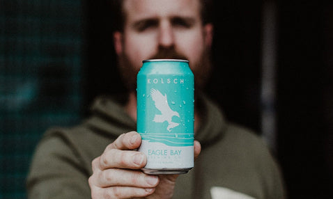 A person holding a Crispy Ice Cold Eagle Bay Brewing Co Kolsch