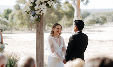 A couple getting married under an altar with white roses in the corner at Eagle Bay Brewing Co's outdoor wedding venue