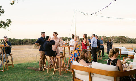 Wedding guests mingling outside and sitting in outdoor furniture as the sun sets at Eagle Bay Brewing Co's wedding venue