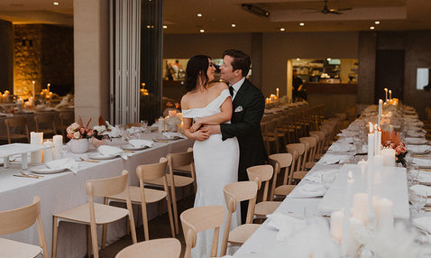 A just-married couple embrace happily inside Eagle Bay's wedding venue, decorated for the wedding reception before guests arrive to sit down