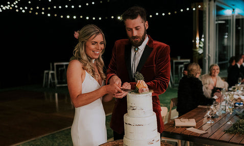 A married couple happily cutting their three tier white cake inside at Eagle Bay's wedding venue