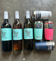 Three wine bottles with turquoise labels and four YETI tumblers on a gray surface.